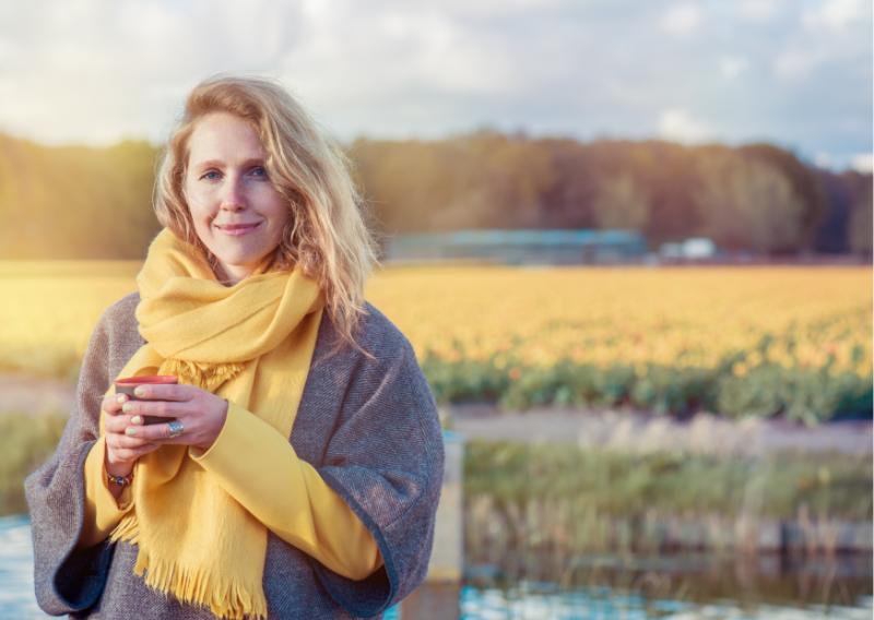 Mujer sonriendo a cámara mientras toma un té en la naturaleza